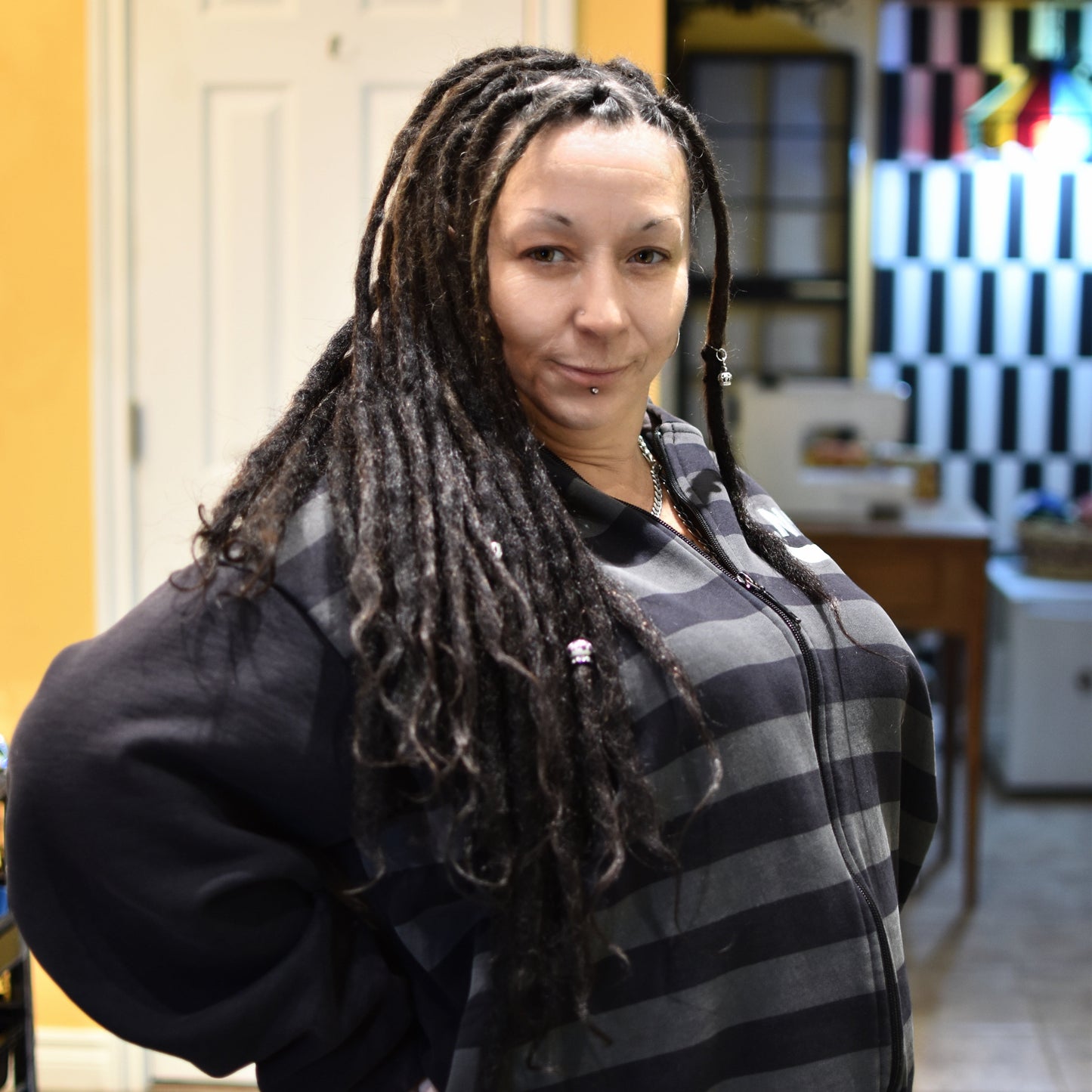 Woman with dreadlocks wearing a black and gray striped sweater in an indoor setting.