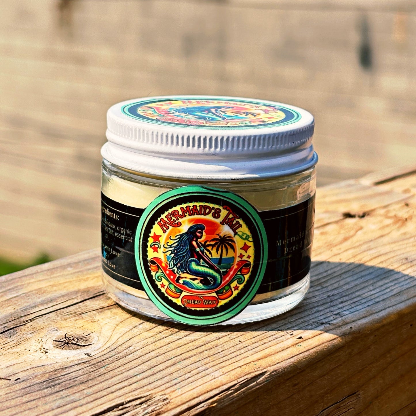 Jar of Mermaid's Tail dread wax with a colorful label on a wooden surface in sunlight