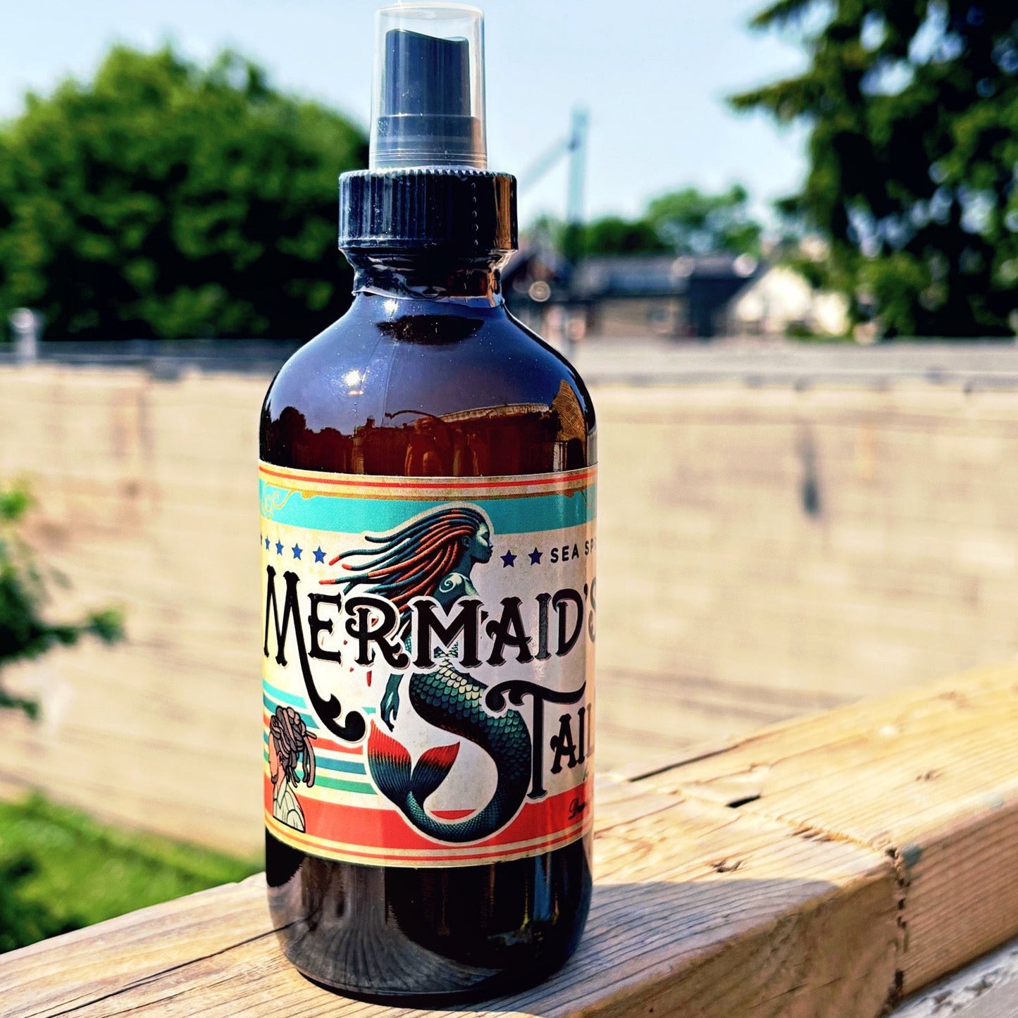 Bottle of 'Mermaid Tail' spray on a wooden surface with a natural background