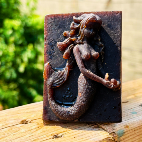 African Black Soap Decorative mermaid shampoo Bar on a wooden surface with a blurred natural background