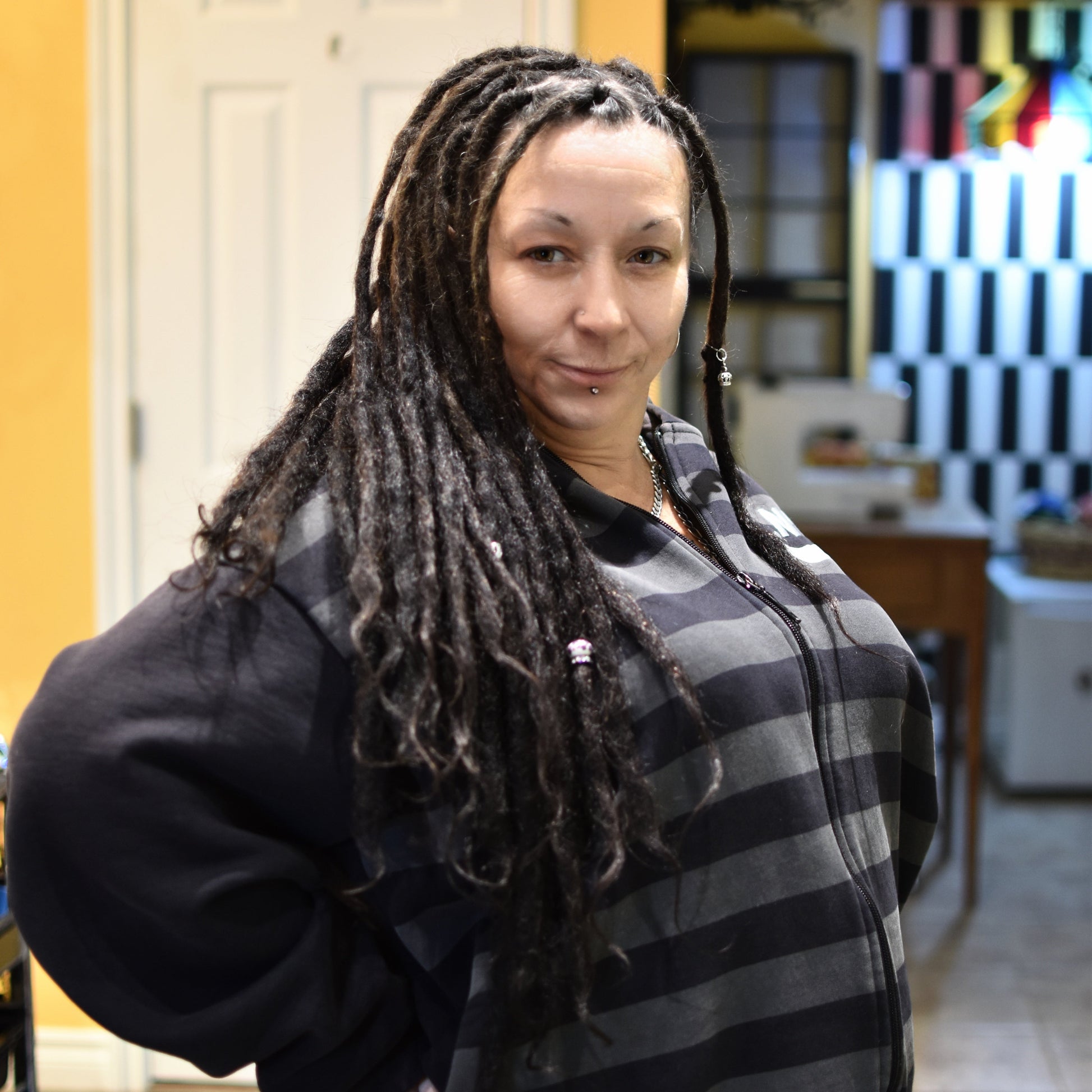 Brenda at Dread Love with dreadlocks wearing a black and gray striped sweater in an indoor setting.