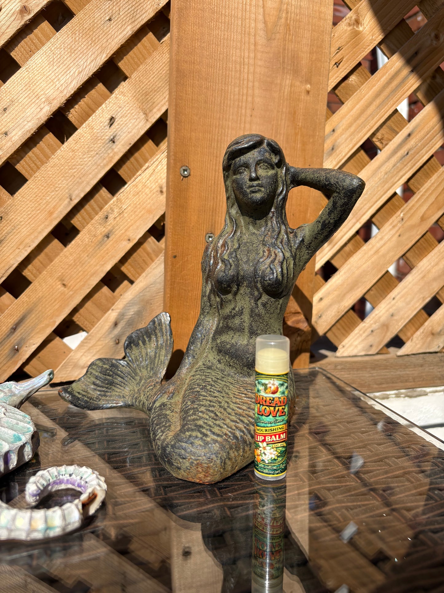 Dread Love Summertime Creamsicle Vegan Nourishing Lip Balm tube on an outdoor table styled with a conch shell, mosaic starfish, and teal dish