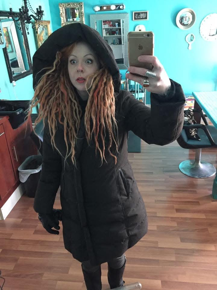 Krista at Dread Love taking a mirror selfie wearing a dark coat in a room with blue walls and wooden floors.