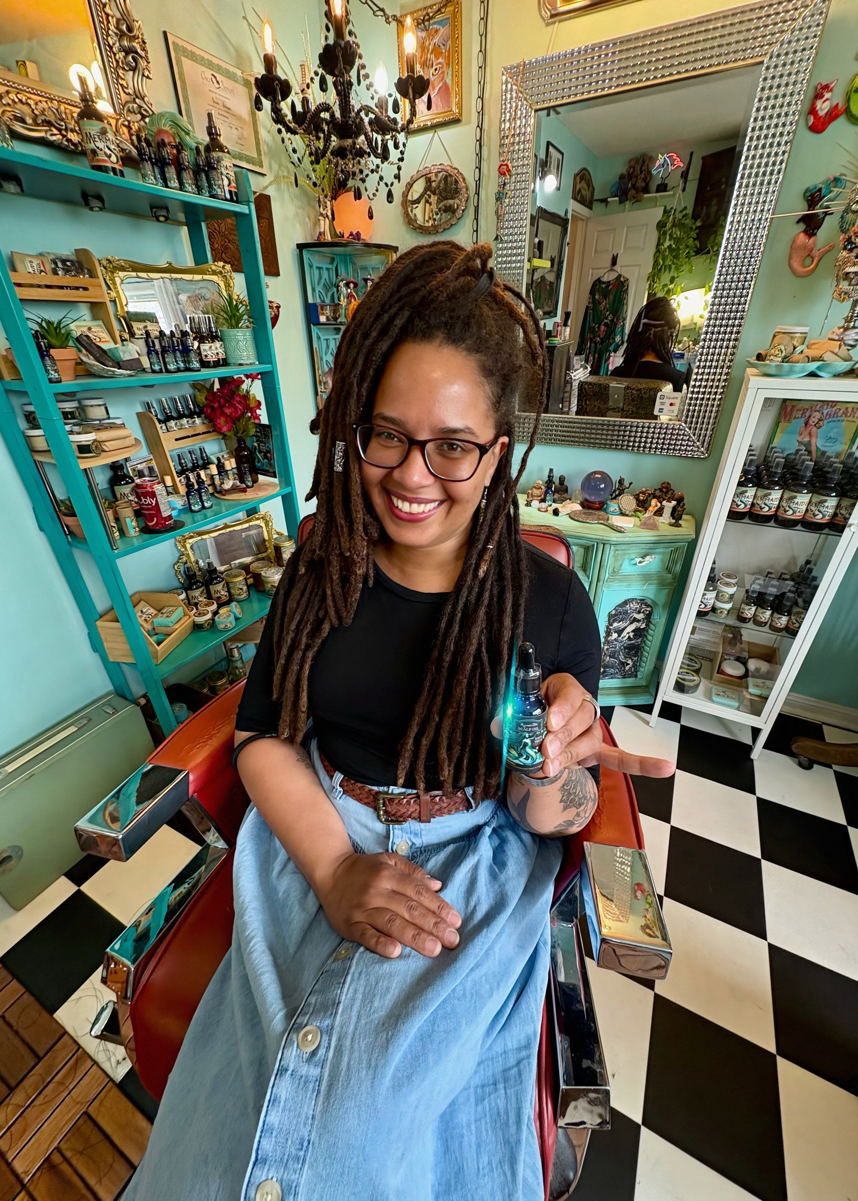 Woman with dreadlocks sitting in a barber chair in a colorful barbershop.