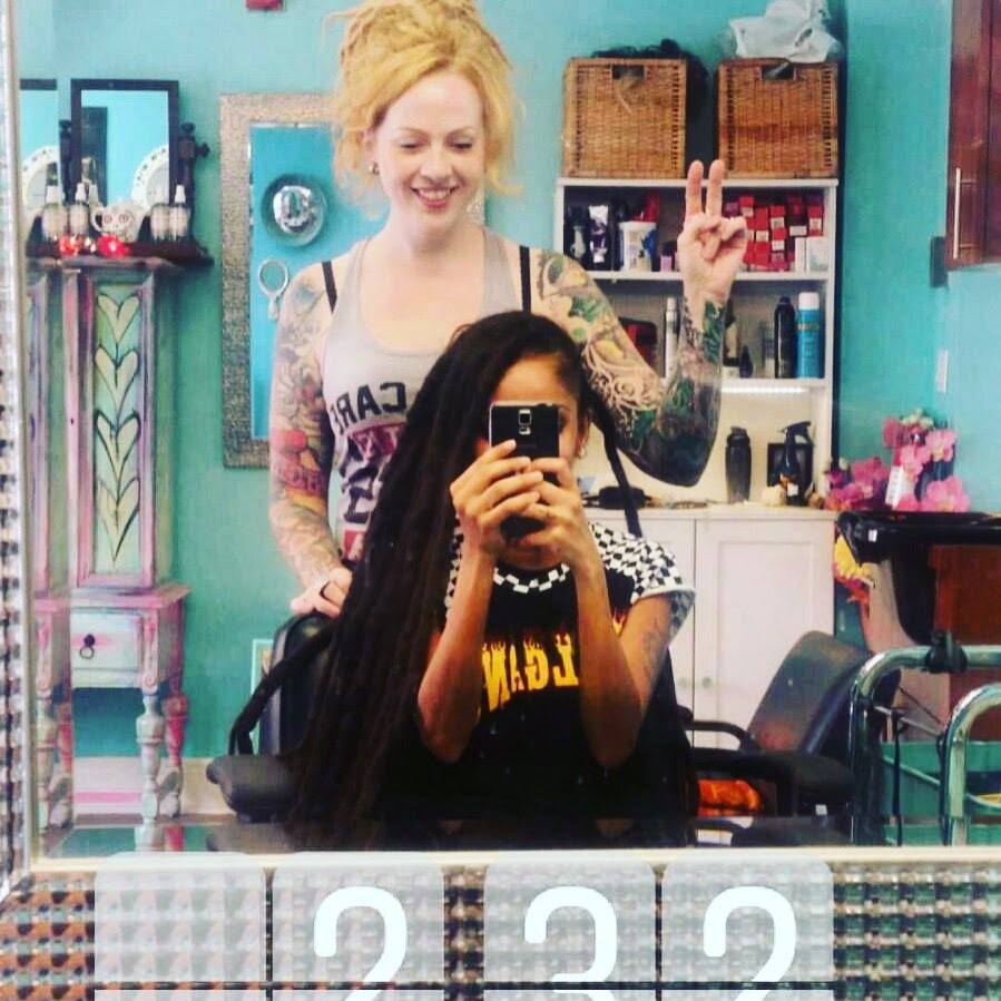 Two women in a dreadlock hair salon with colorful decor and products.