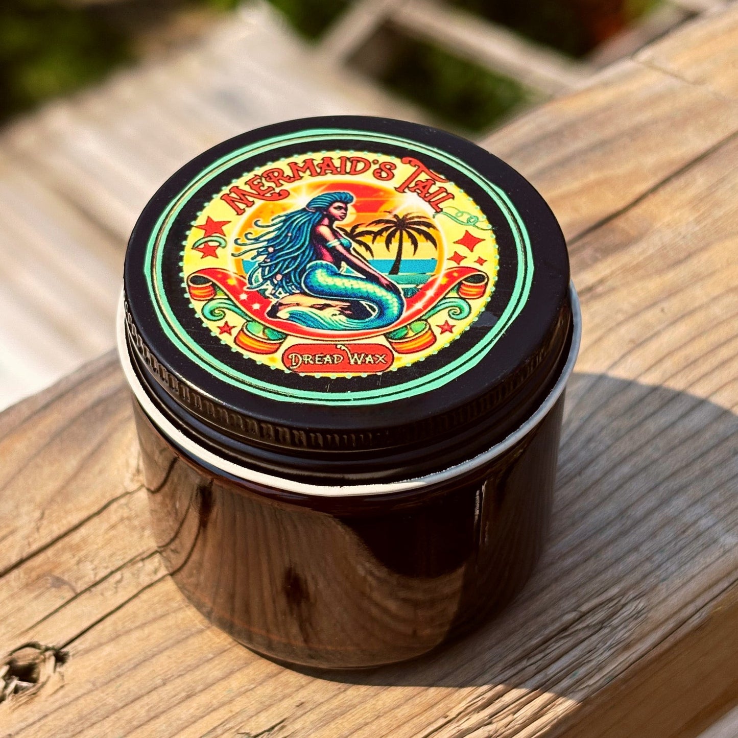Jar of 'Mermaid's Tail' pigmented dread wax  on a wooden surface with a colorful label featuring a mermaid.